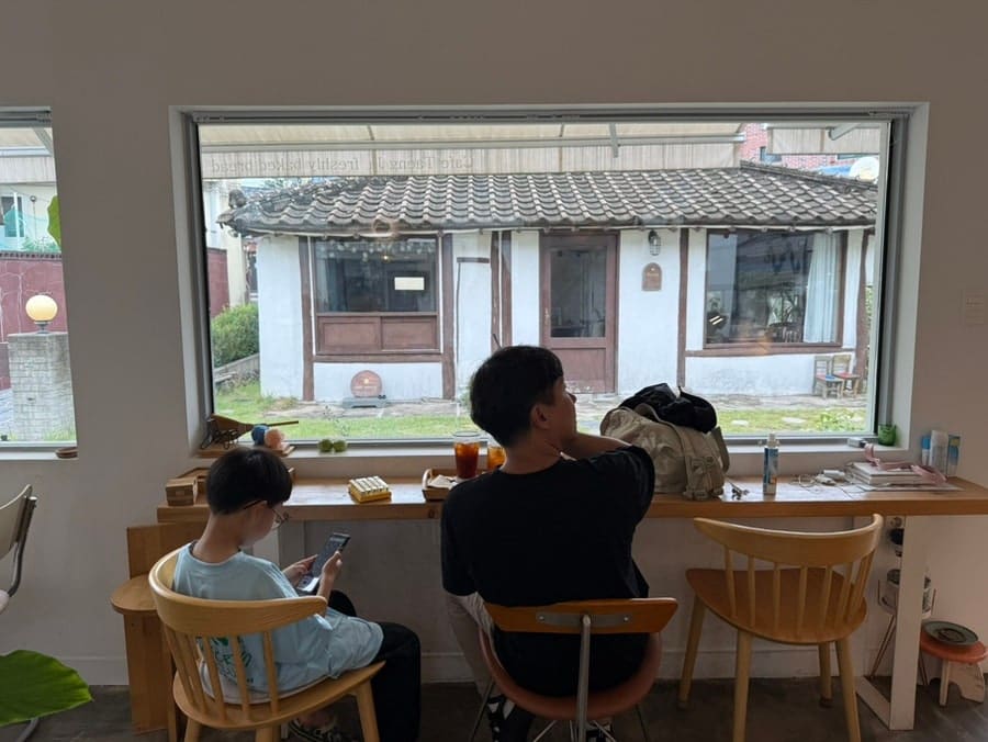 같은 블로거가 카페 마당과 그 창 안쪽에서 담은 두 장입니다. 낮은 돌담과 우체통, 마당의 조약돌 길이 옛집의 흔적을 그대로 보여주고,