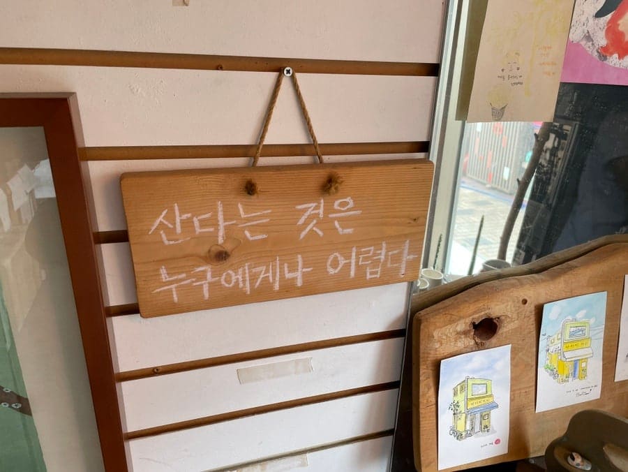 uuzaen이 남긴 사진입니다. 나무 진열장 위에 노란 외벽 건물을 그린 그림엽서가 놓여 있고, 옆에는 로스팅 도구와 9월 달력이 함께 보입니다.