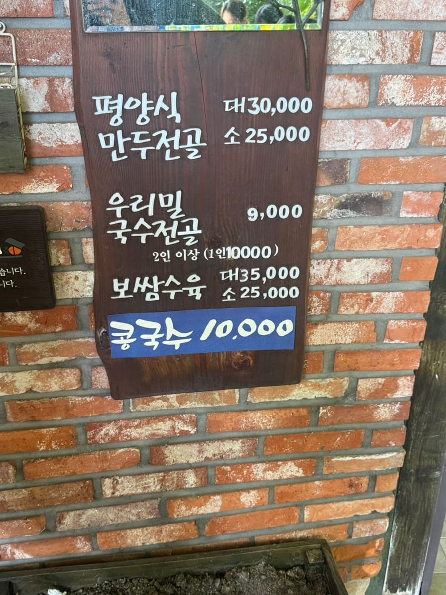 0123shop이 찍은 입구 유리문입니다. '고가네칼국수'라는 글자가 새겨진 유리 너머로 초록빛 마당과 담쟁이가 우거진 벽이 보입니다.