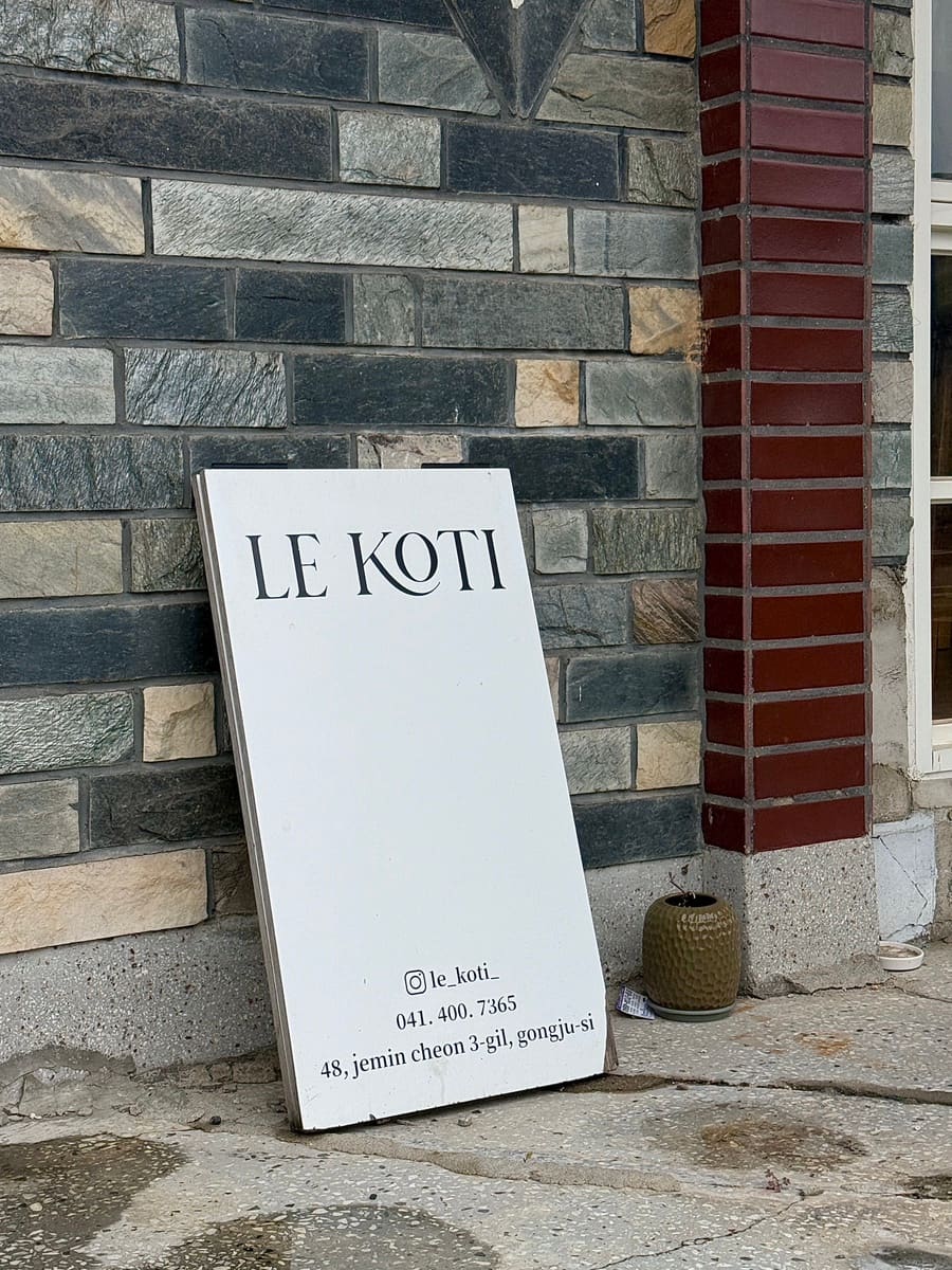 sksgp가 찍은 입간판입니다. 돌벽에 기대 세운 흰 간판에 'LE KOTI'와 주소가 단정한 서체로 적혀 있습니다.