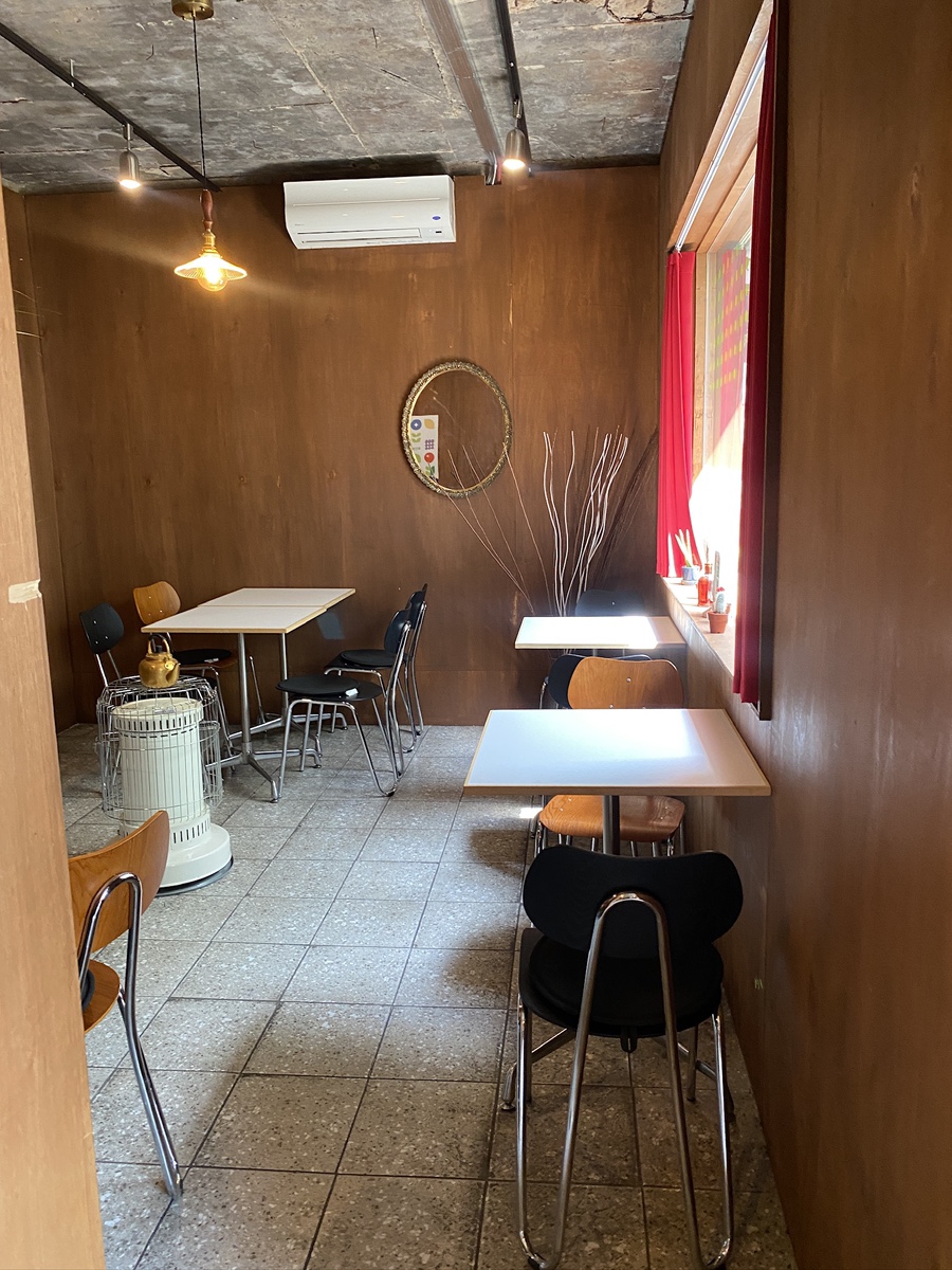 같은 카페의 넓은 실내를 담은 사진입니다. 붉은 커튼 사이로 든 낮빛과, 거친 천장 아래 놓인 낡은 의자들이 대비를 이룹니다.