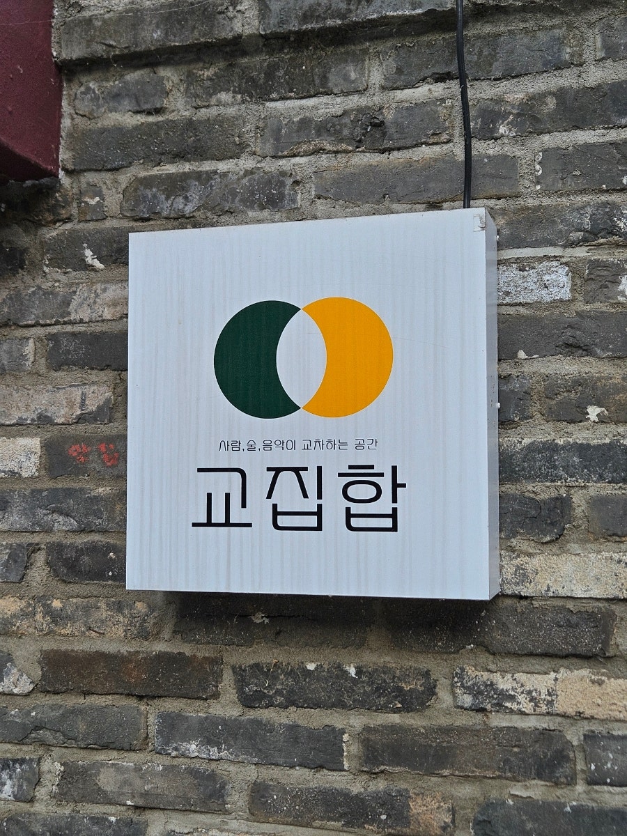 같은 가게의 간판을 가까이서 담은 사진입니다. 거친 벽돌 벽에 매단 깔끔한 간판이 도드라져, 오래된 뼈대 위에 새로운 쓰임을 얹은 흔적이 또렷합니다.