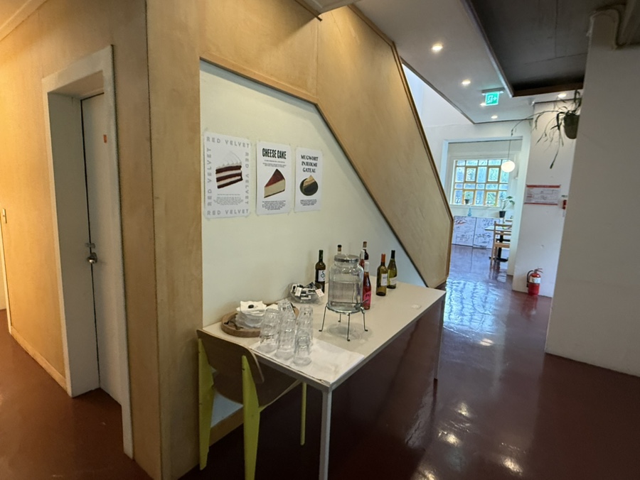 계단 아래 작은 공간을 담은 사진입니다. 케이크 종류를 소개한 안내지와 가지런히 놓인 유리잔들이, 식사 뒤에 디저트까지 챙기는 손님들의 동선을 짐작하게 합니다.