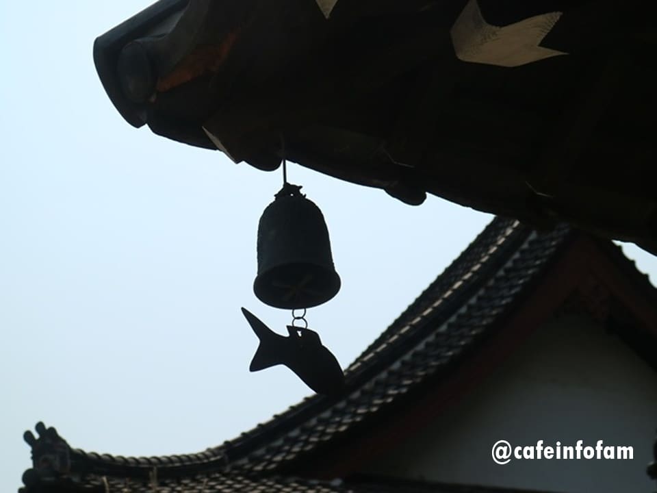 cafeinfofam이 찍은 처마 아래 풍경과 마당의 꽃나무입니다. 물고기 모양 장식이 매달린 종의 실루엣,