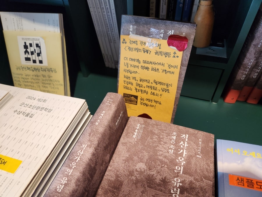 같은 사람이 찍은 책장과 진열대입니다. 군산을 배경으로 한 소설 '적산가옥의 유령'이 손글씨 추천 카드와 함께 놓여 있고,
