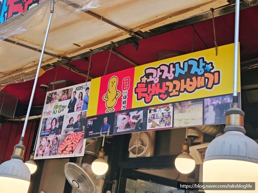 광장시장의 입구를 포함한 전경. 오래된 간판과 새로운 표지판이 겹쳐 있는 장면에서 시장의 오랜 역사가 읽힙니다. 여러 세대가 이곳을 지나왔습니다.