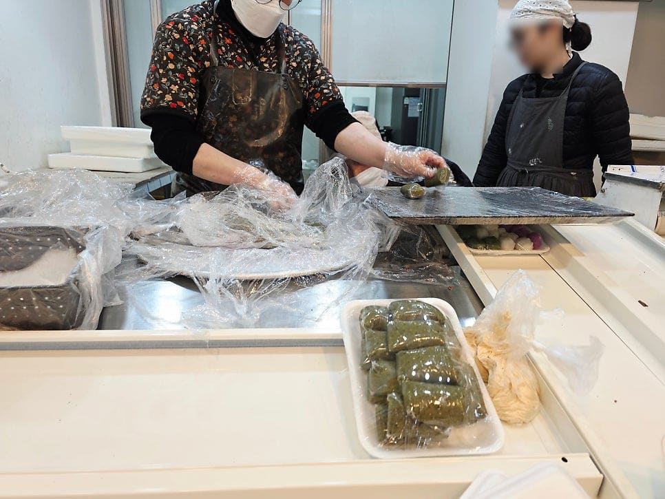 60년 잡할머니 좌판에서 해산물을 다루는 손과, 옆 가게에서 나물을 계속 포장하는 손입니다. 손님이 몰리기 전 이른 시간에도 손은 쉬지 않고 움직입니다.