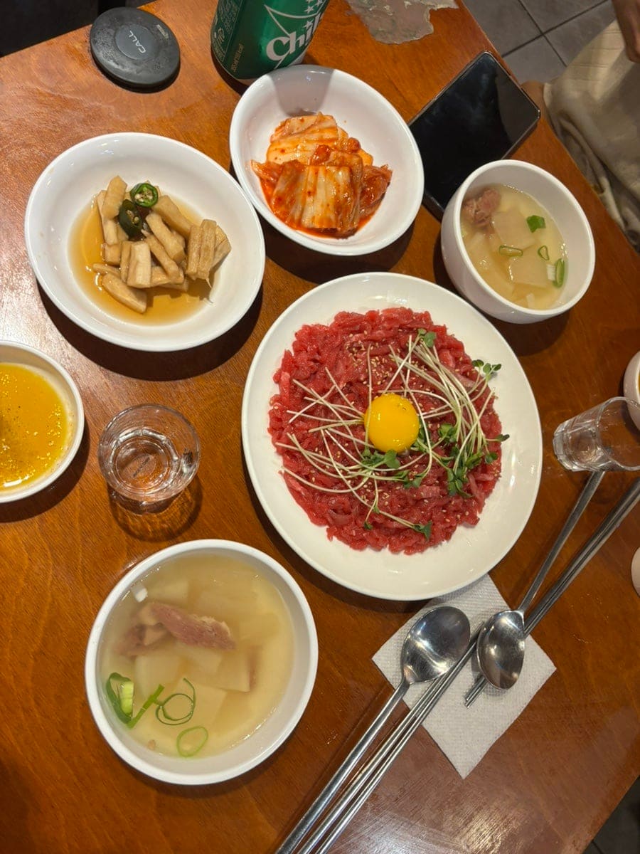 육회와 반찬들이 상 위에 가득 채워진 모습입니다. 노른자를 얹은 육회 한 접시에 곰탕과 밑반찬까지,