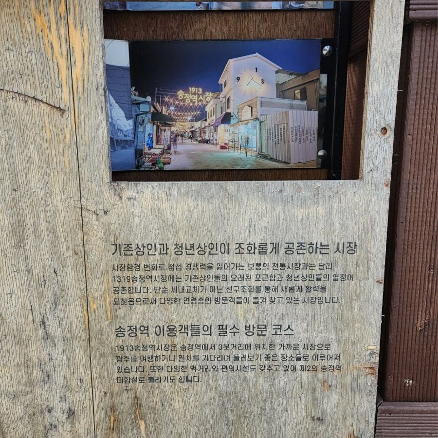 lsl652님이 시장 골목에서 발견한 안내판입니다. 나무 벽에 걸린 사진 속에는 시계탑에 불이 켜진 밤의 시장 풍경이 담겨 있고,