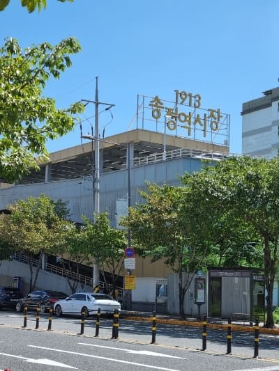 wlsa7님이 공영주차장 쪽에서 시장으로 들어서며 남긴 사진입니다. 나무 사이로 1913송정역시장이라 적힌 옥상 간판이 보이고, 모퉁이를 돌면 또 다른 아치형 입구가 나타납니다.