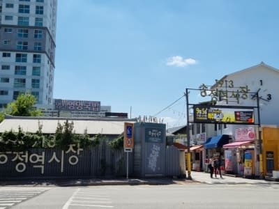 wlsa7님이 공영주차장 쪽에서 시장으로 들어서며 남긴 사진입니다. 나무 사이로 1913송정역시장이라 적힌 옥상 간판이 보이고, 모퉁이를 돌면 또 다른 아치형 입구가 나타납니다.