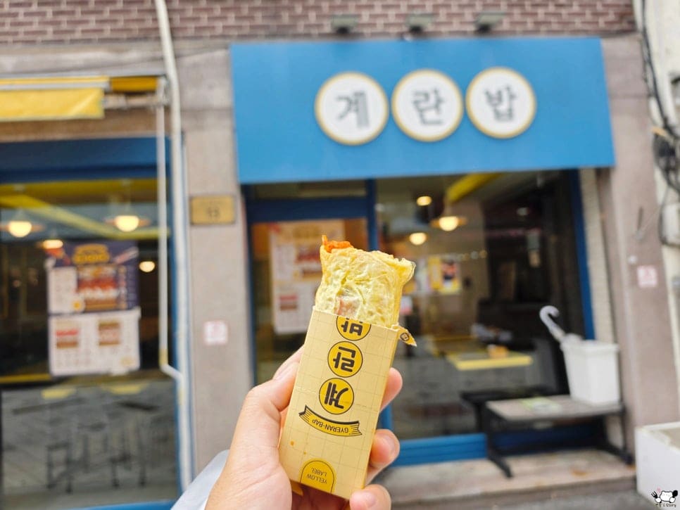 you9013593님이 포장한 계란밥을 들고 매장 앞에서 남긴 사진입니다. 파란 간판에 하얀 동그라미 세 개로 적힌 계란·란·밥 글자가 뒤로 보이고,