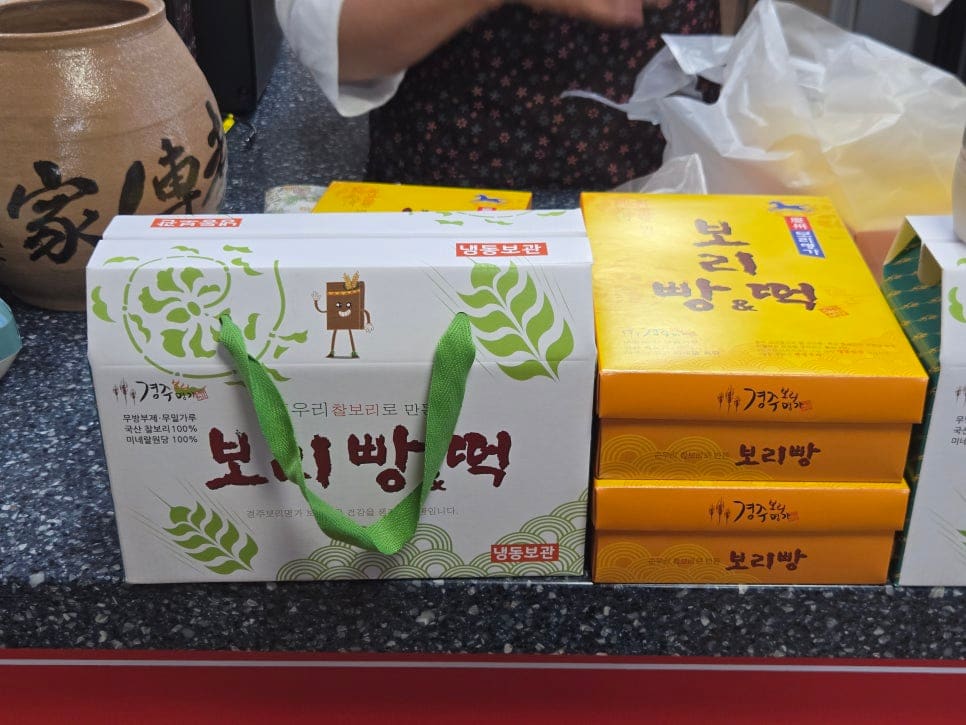 vely_hyun1621이 담은 포장 상자와, aquair1009이 한 입 베어 문 찰보리빵입니다. 팥소 없이 보리 자체의 결만 남은 단면이 이 집의 특징을 보여줍니다.