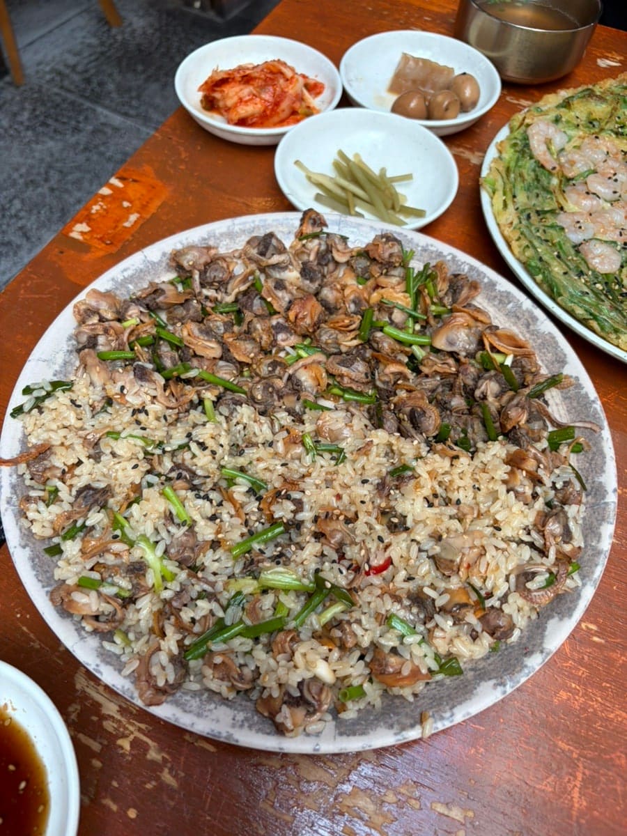 ohanazip이 남긴 꼬막무침비빔밥과 해물파전입니다. 꼬막과 밥알이 반반씩 섞여 그릇을 가득 채운 비빔밥과, 새우가 통째로 올라간 파전을 한 상에 함께 두고 찍었습니다.