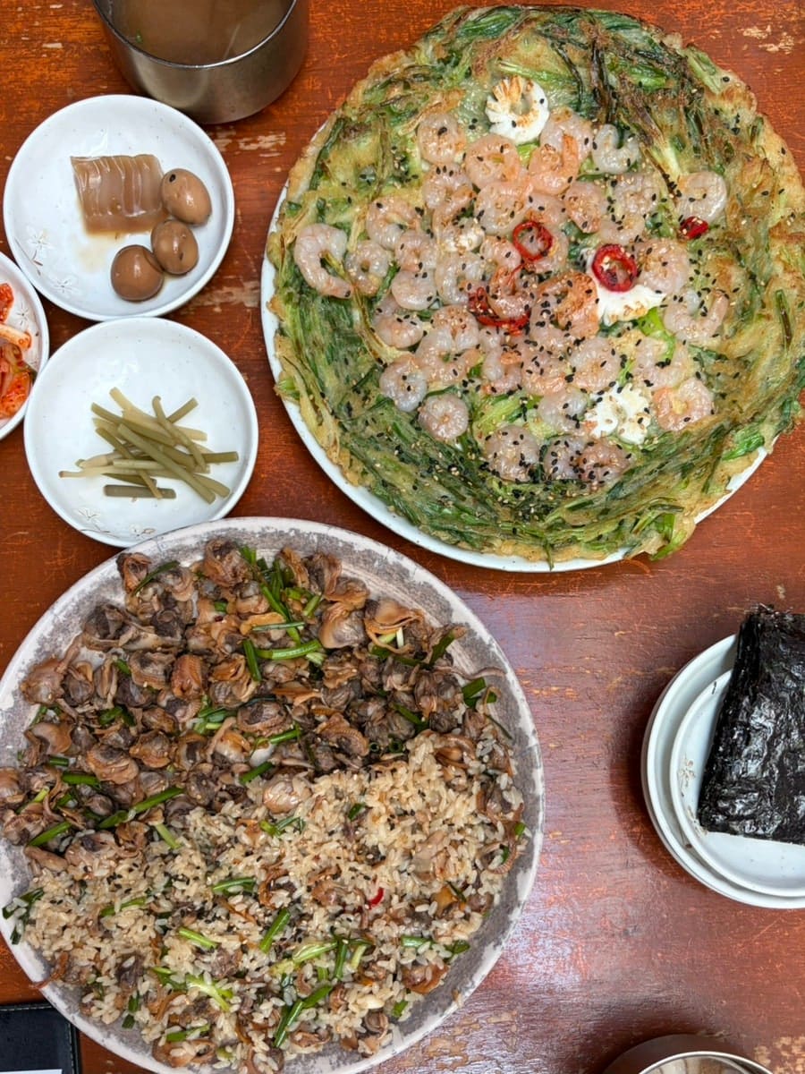 ohanazip이 남긴 꼬막무침비빔밥과 해물파전입니다. 꼬막과 밥알이 반반씩 섞여 그릇을 가득 채운 비빔밥과, 새우가 통째로 올라간 파전을 한 상에 함께 두고 찍었습니다.