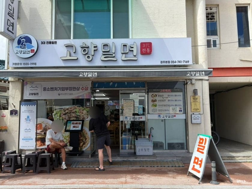baginamul이 담은 고향밀면 외관과, 문 앞에 붙은 손글씨 안내문입니다. '경주 밀면의 원조 백년가게'라는 문구와 함께 웨이팅 등록법,