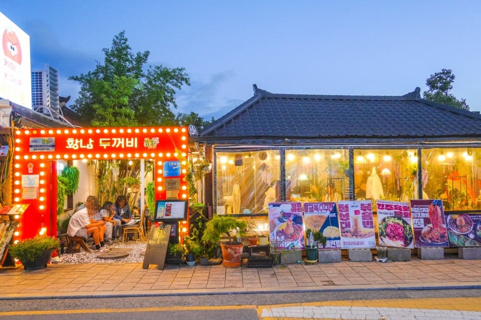 mixsun이 담은 황남두꺼비식당의 붉은 알전구 간판입니다. 해질녘 환하게 불을 밝힌 전경과, 방송 출연 사실을 알리는 안내판이 걸린 간판 클로즈업을 함께 보여줍니다.