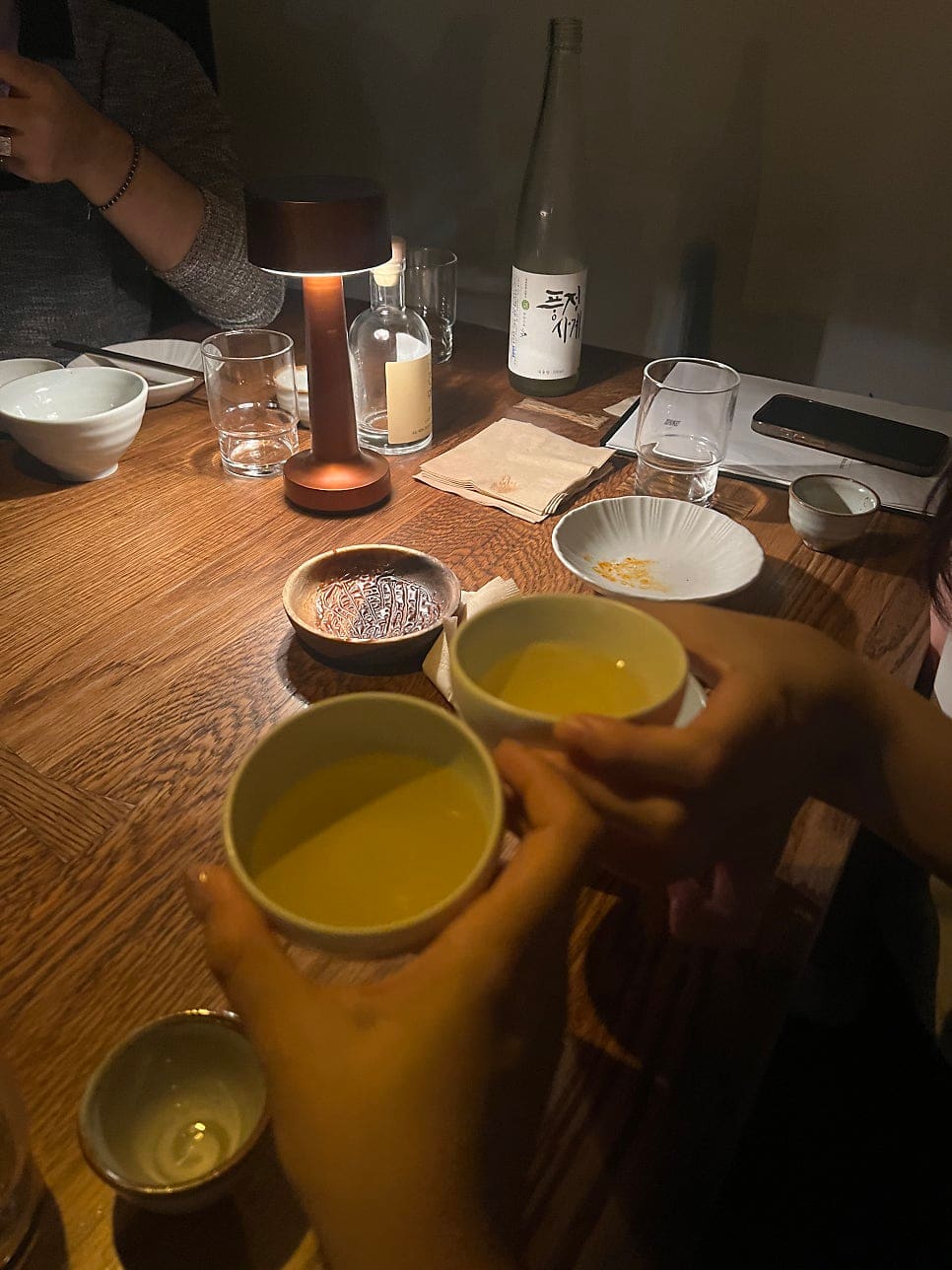 chacha_archive님이 남긴 사진입니다. 그림이 그려진 시그니처 막걸리 병과 나란히 놓인 다섯 개의 잔, 그리고 낮은 조명 아래 서로 잔을 부딪히는 손까지,