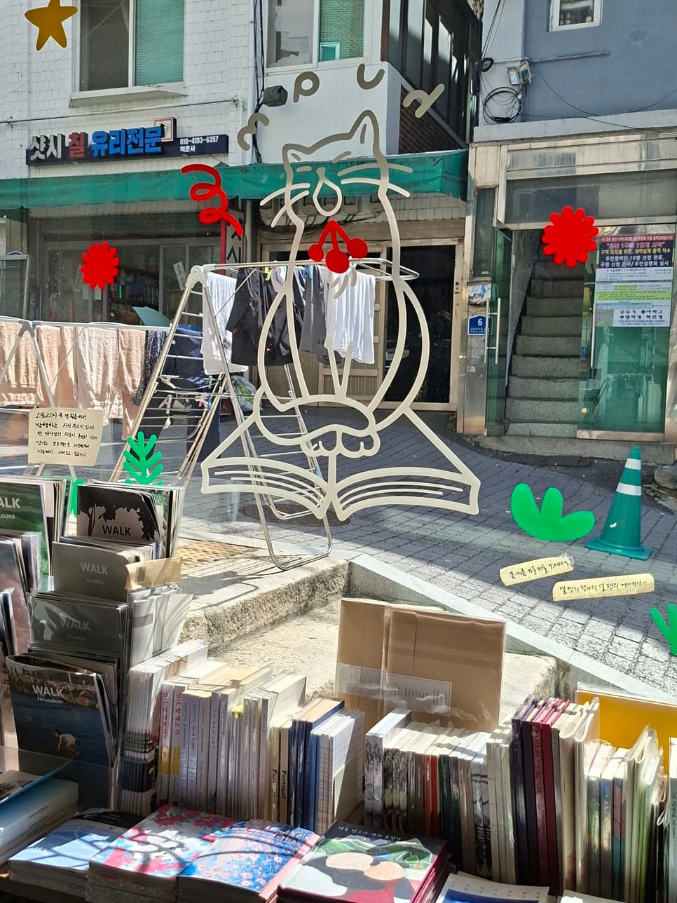 카페 다포딜 창가에 앉으면 유리에 붙은 고양이·꽃 스티커 너머로 바로 아래 좁은 골목이 내려다보입니다. 유리 철물점 간판과 계단,