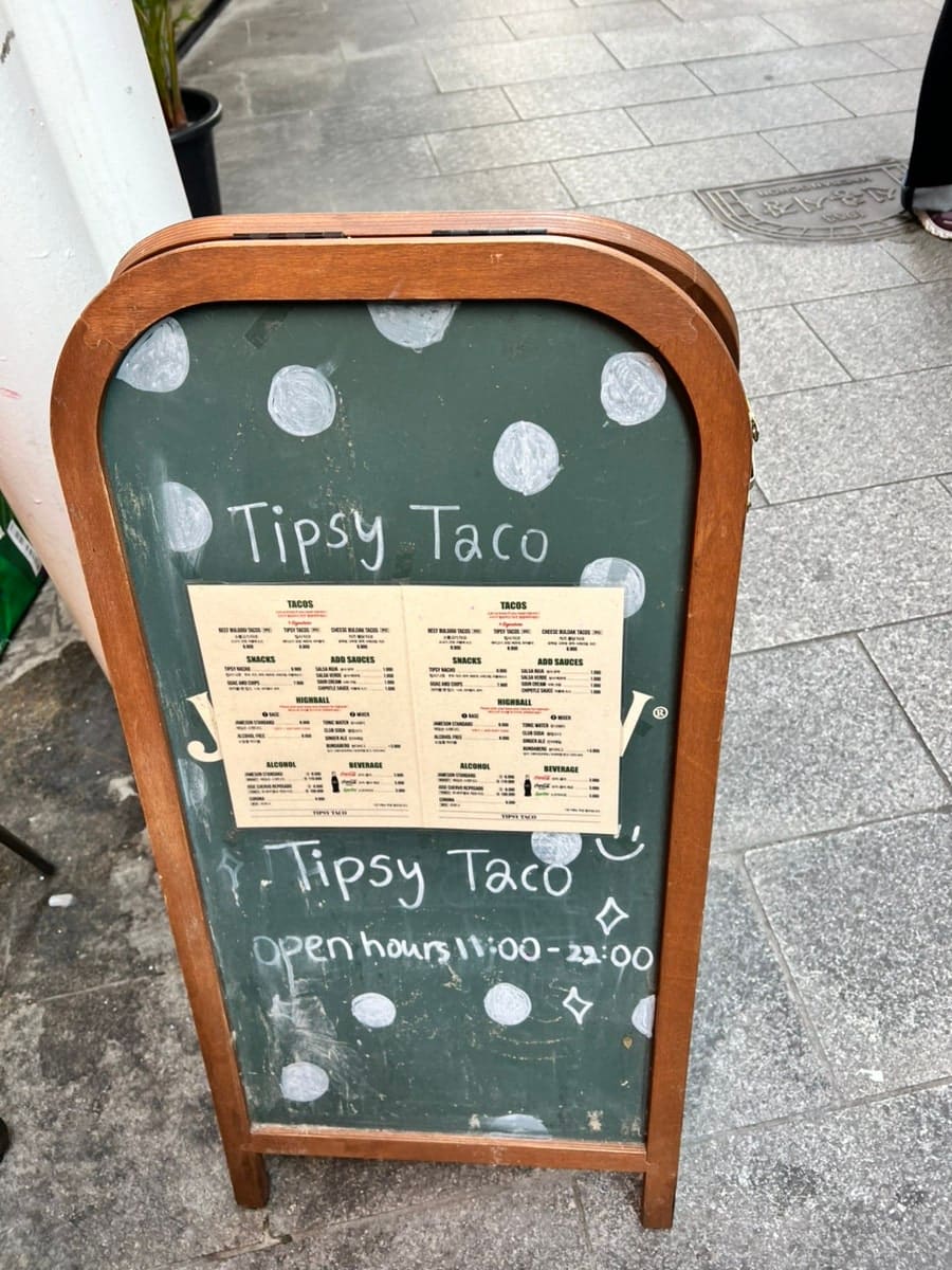 물방울무늬 칠판 입간판에 타코 메뉴판이 붙어 있고, 창가 자리엔 포크와 나이프가 냅킨 위에 가지런히 놓여 있습니다.
