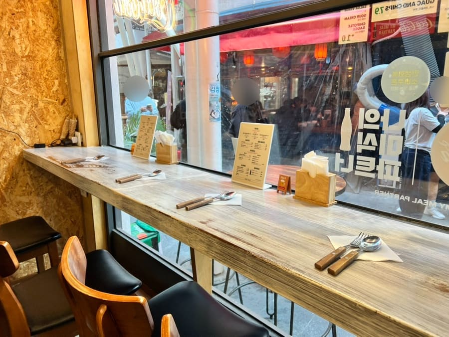 물방울무늬 칠판 입간판에 타코 메뉴판이 붙어 있고, 창가 자리엔 포크와 나이프가 냅킨 위에 가지런히 놓여 있습니다.