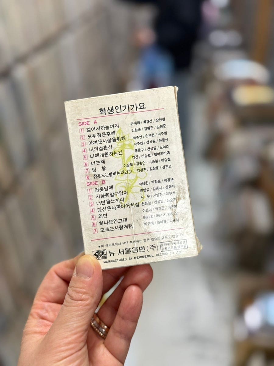 wlduql0708이 촬영한 가게 앞 옛 카세트테이프입니다. 손 글씨처럼 인쇄된 수록곡 목록과 빛바랜 가수 사진이 그대로 남아 있어,