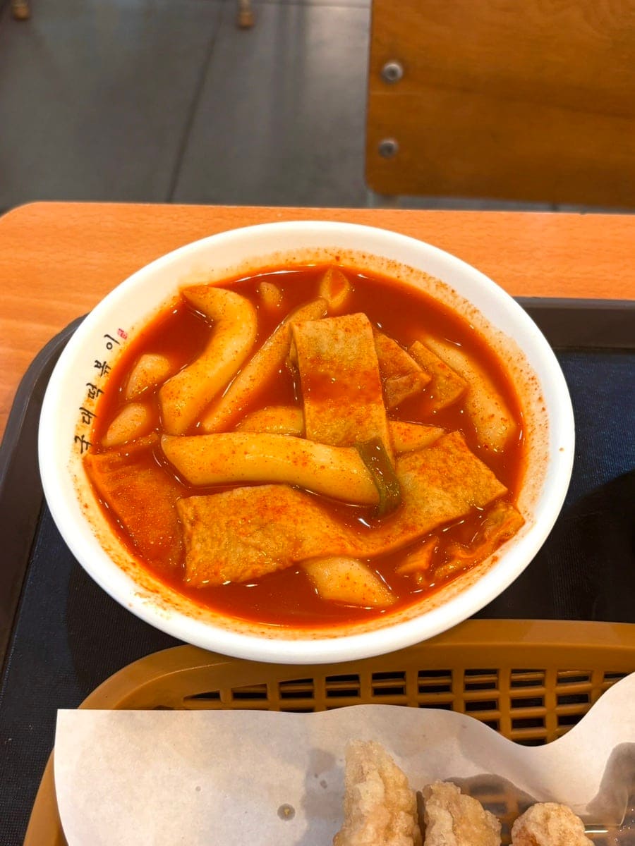 cherrieee_는 청계천 산책 후 이마트 청계천점에 들러 떡볶이 1인분과 오징어튀김을 주문했습니다. 나무 식탁 위 쟁반에는 텐까스를 얹은 국물떡볶이와 오뎅 국물 냄비,