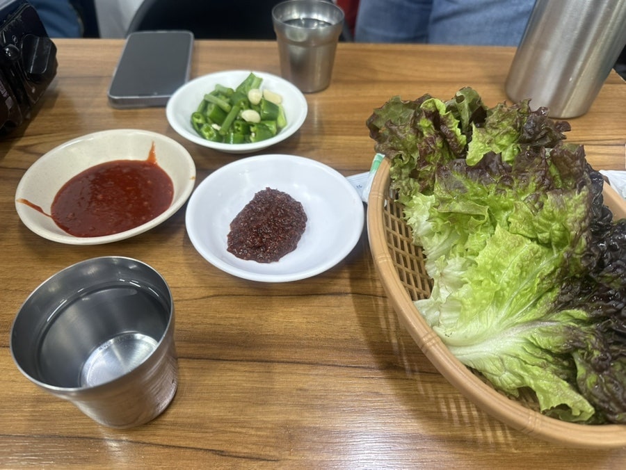 travel_me가 촬영한 상차림과 포일에 담긴 야채곱창입니다. 스테인리스 컵과 쌈채소 바구니가 놓인 테이블 위로,