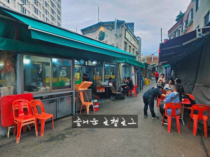 fhcp가 촬영한 전봇대곱창 외관과 저녁 야장입니다. 낮에 본 노란 간판과 달리, 저녁에는 파란 천막 아래 빨간 플라스틱 의자들이 놓이고 사람들이 골목을 채웁니다.