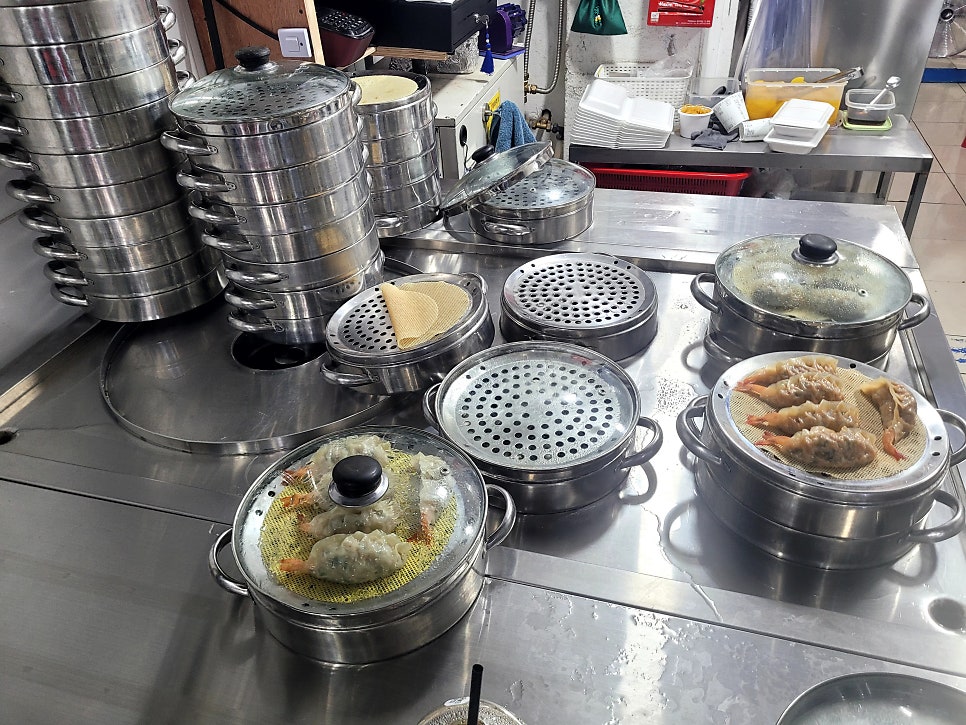 gkdudtjr2가 촬영한 스테인리스 찜기들과 조리대입니다. 여러 겹으로 쌓인 찜기 사이로 새우만두가 삼베 위에 올려져 있고,
