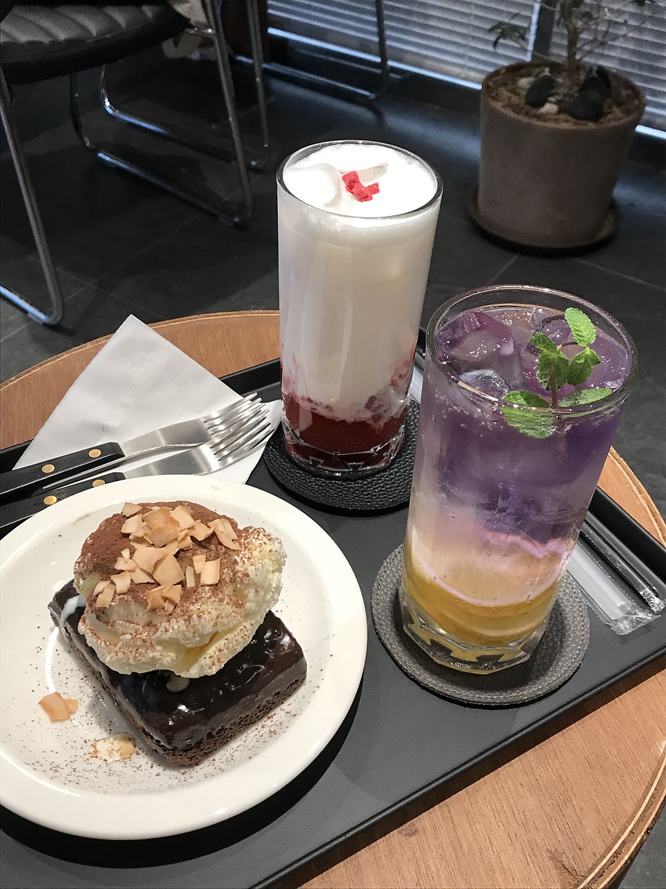 seyun0403_가 촬영한 테라스에서 내다본 거리 풍경과 브라우니, 음료입니다. 흰색 철제 테이블과 의자가 놓인 테라스 너머로 동네 풍경이 보이고,