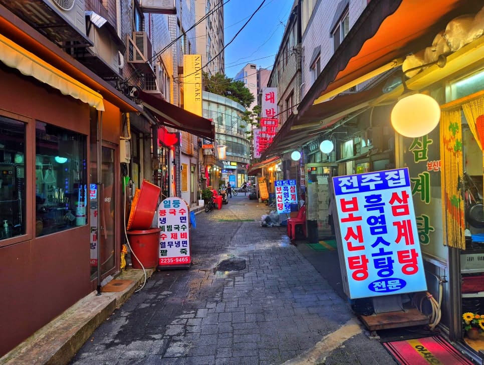 jhbluesss가 해 질 녘에 촬영한 골목 풍경입니다. 색색의 전구 줄과 네온 간판이 하나둘 켜지며, 낮 동안 조용하던 거리가 사람들의 말소리로 채워지기 시작합니다.