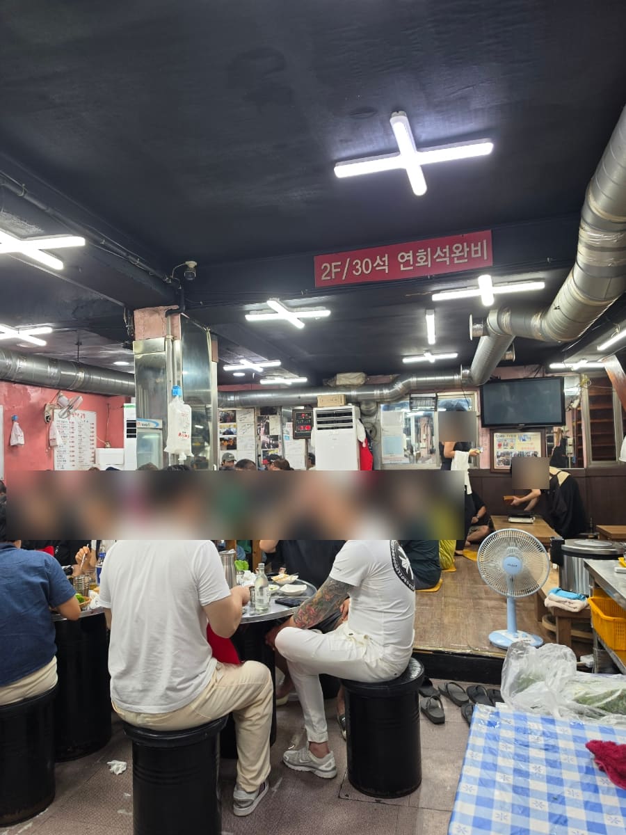 qoowoo_가 촬영한 출입문의 영업시간 안내와 2층 홀입니다. 오전 10시부터 다음 날 오전 6시까지라는 안내문 아래로, 2층 연회석까지 사람들로 가득 차 있습니다.