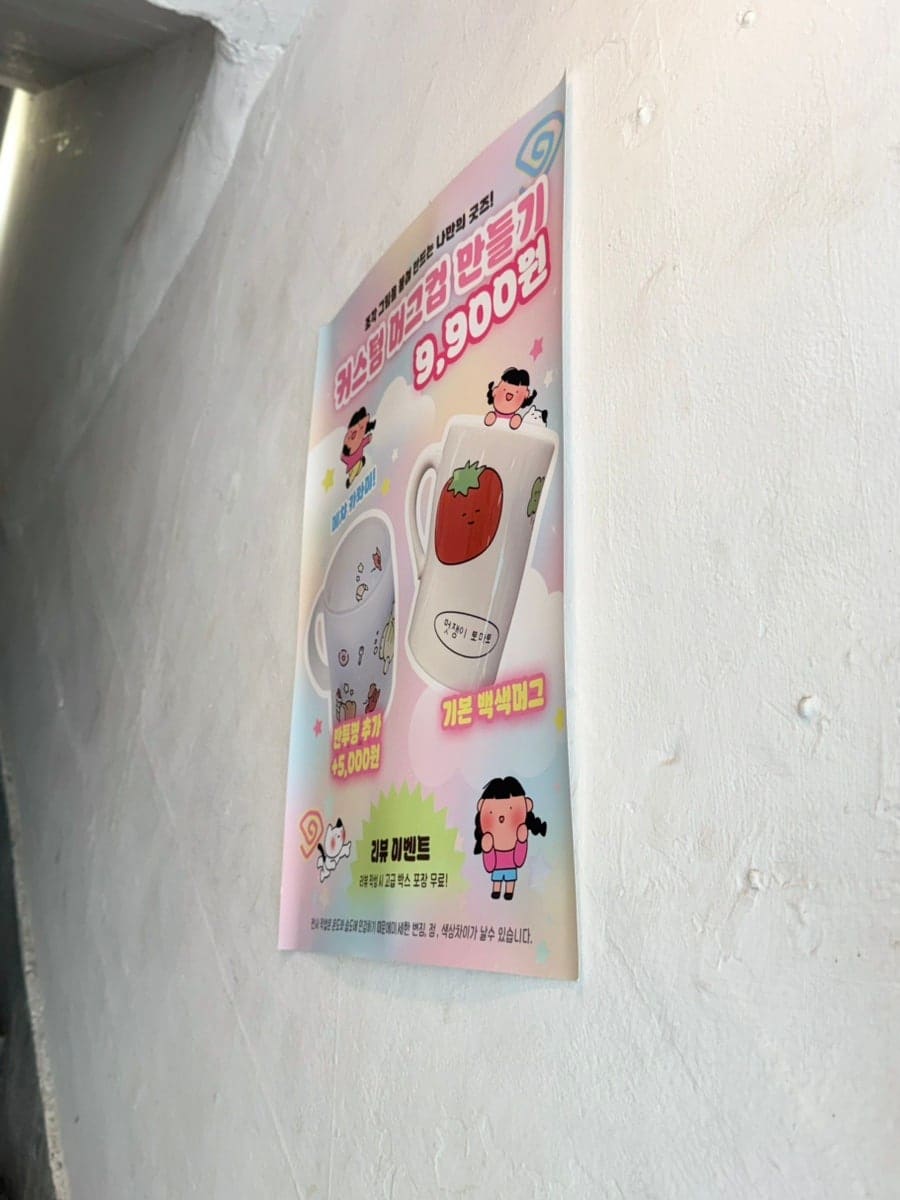 공방 입구의 가격 안내 포스터입니다. 분홍색 배경에 '끄적끄적미술공방 9,900원', 귀여운 딸기와 여자 아이 일러스트가 있으며, 다양한 체험 프로그램과 가격을 안내하고 있습니다.