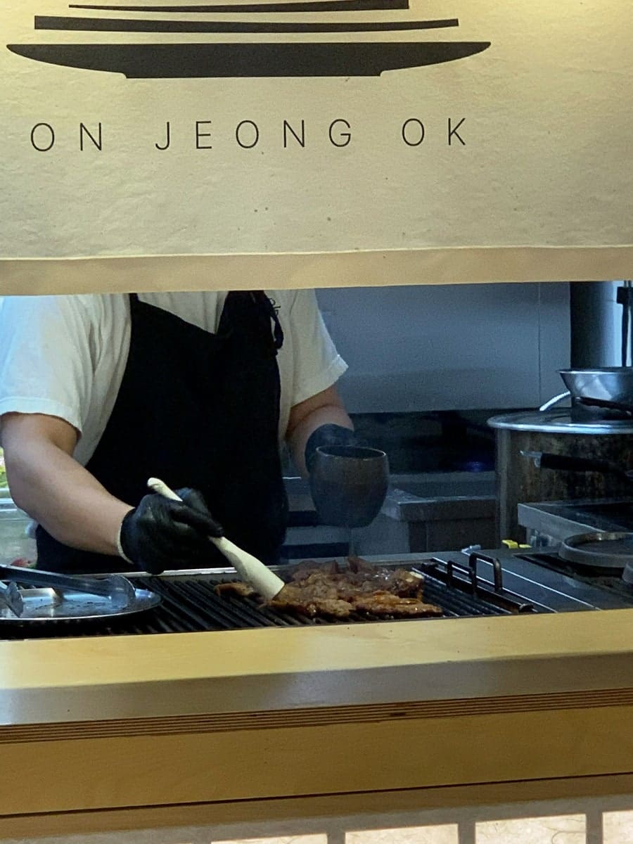 zebra_context는 주방 창 너머로 직원이 숯불 위에서 갈비를 붓으로 발라 가며 굽는 장면을 포착했습니다.