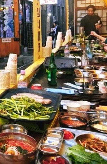 cingco는 인사동부터 익선동까지 걸어와 이 집에서 저녁을 먹었습니다. 불판 가득 미나리와 반찬이 차려진 야장 테이블과, 가위질 전 두툼한 생삼겹살 한 접시를 찍었습니다.
