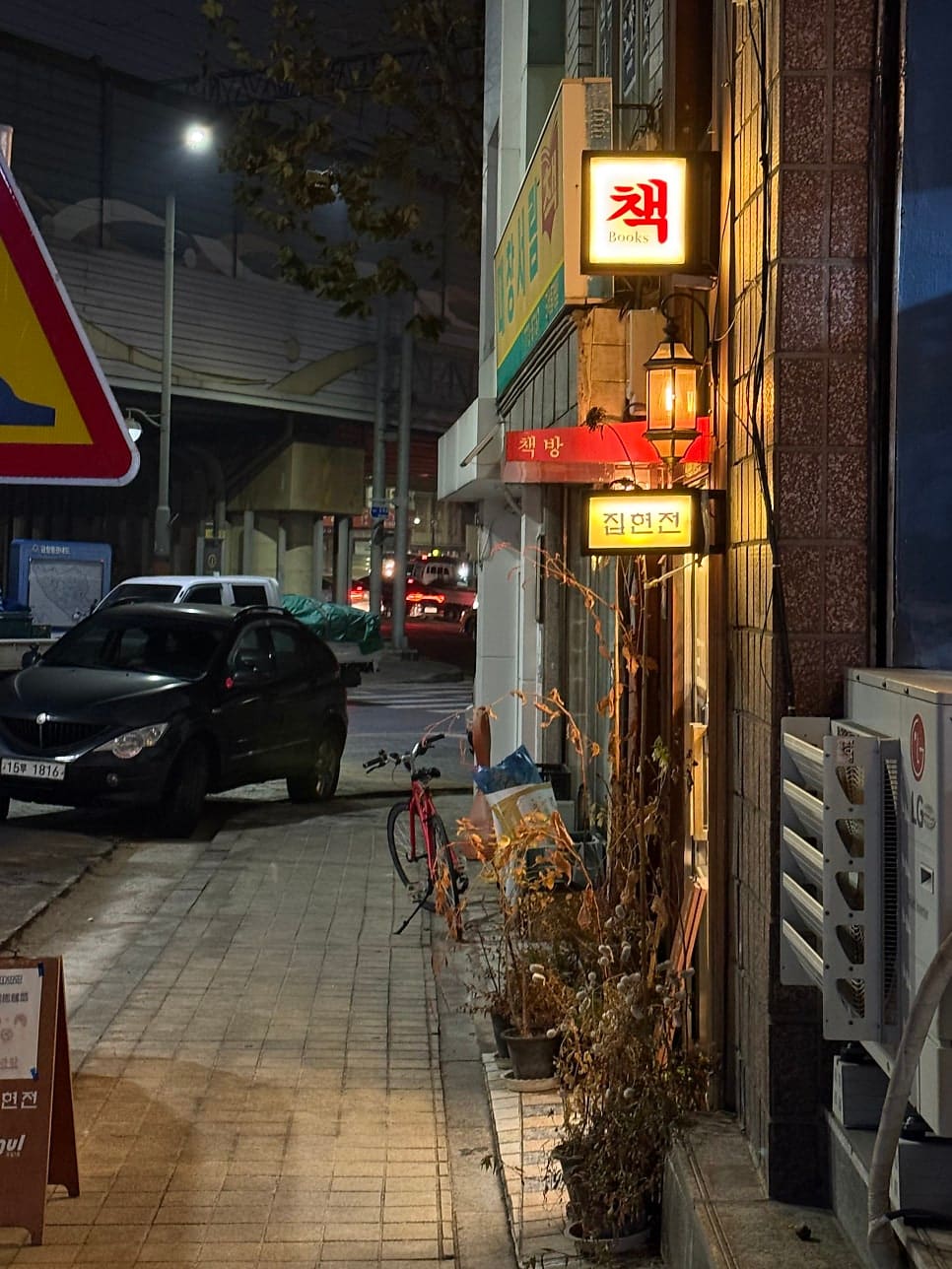 저녁이 내려앉은 골목, 집현전과 아벨책방의 불빛이 좁은 인도를 비춘다. 자전거 한 대와 화분들이 문 앞을 지키고 있다.
