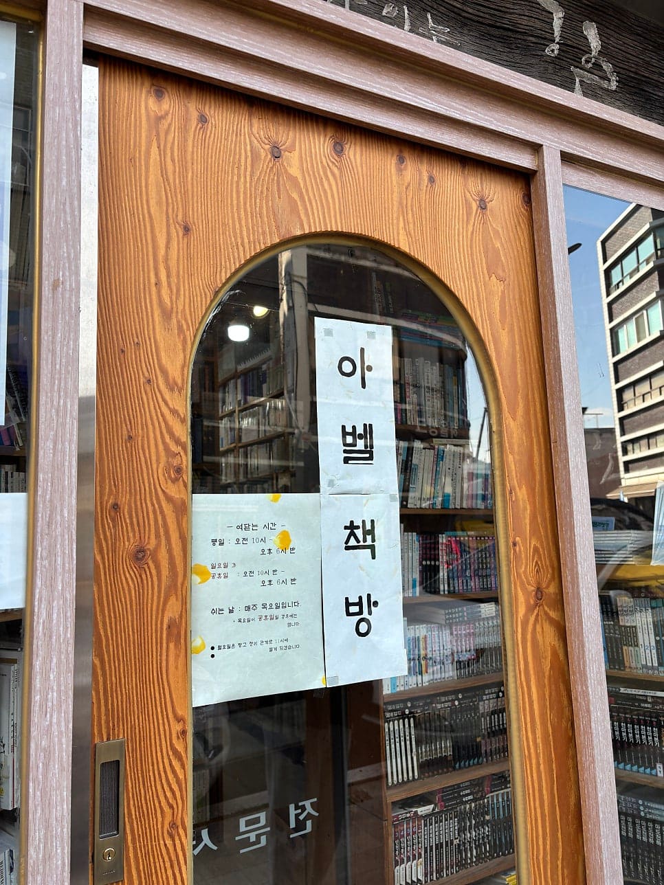 노란 벽돌 건물 아래 나무 책장이 통째로 거리를 향해 열려 있는 아벨서점의 낮 풍경과, 옆 아벨책방의 아치형 나무문.