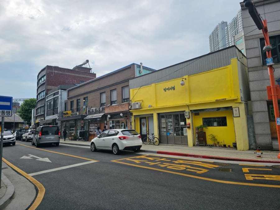 노란 외벽에 since 1953이 적힌 한미서점과 그 앞을 지나는 차들. 오래된 상가 건물들이 나란히 이어진 지금의 골목 풍경이다.