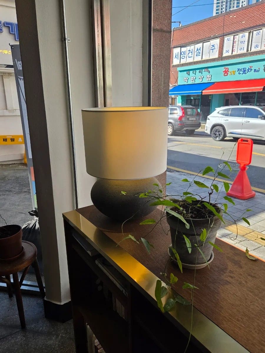 그레이스정이 담은 창가 자리입니다. 오래된 자개장 위 스탠드 조명과 작은 화분, 그리고 창밖으로 마주 보이는 골목 간판까지, 카페 이름처럼 동양적인 정취가 묻어난다고 적었습니다.