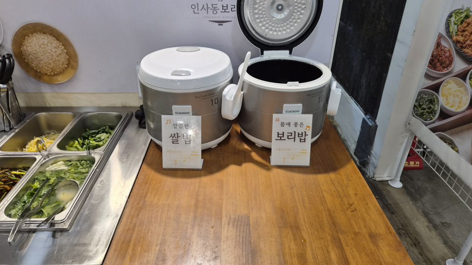 hs010195는 '쌀밥'과 '보리밥' 팻말이 붙은 밥솥 두 개와, 그 옆 보리숭늉 코너를 함께 찍었습니다.