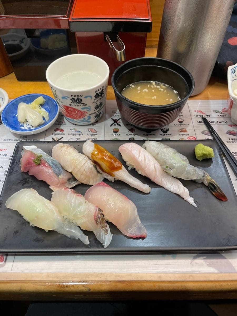 fastsnail333(빠른달팽이)이 담은 입구 조형물과 초밥 접시입니다. 붉은 참치를 쥔 거대한 손 모형이 입구를 지키고 있고, 흰살생선과 제주 생선,