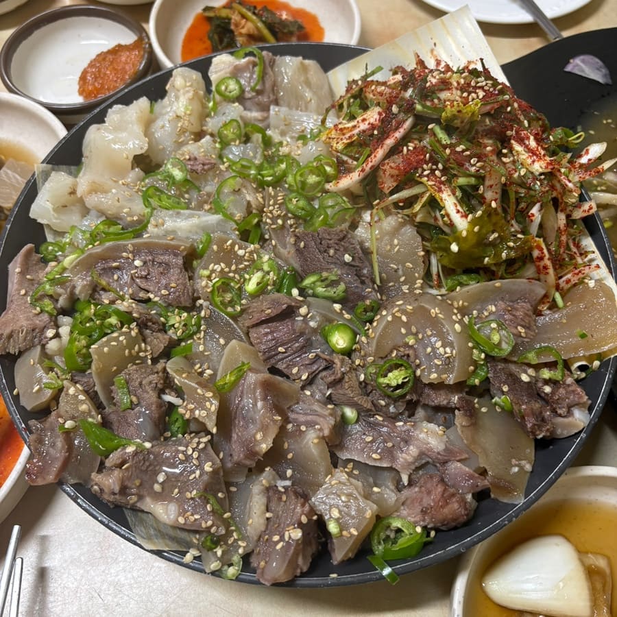 chxown이 담은 반반수육 접시와 한 상 전체입니다. 도가니와 소머리가 절반씩 나뉘어 쌓이고 그 위로 파무침과 깨가 넉넉히 얹혀 있으며, 곁으로 육회 무침과 맑은 탕 두 그릇,