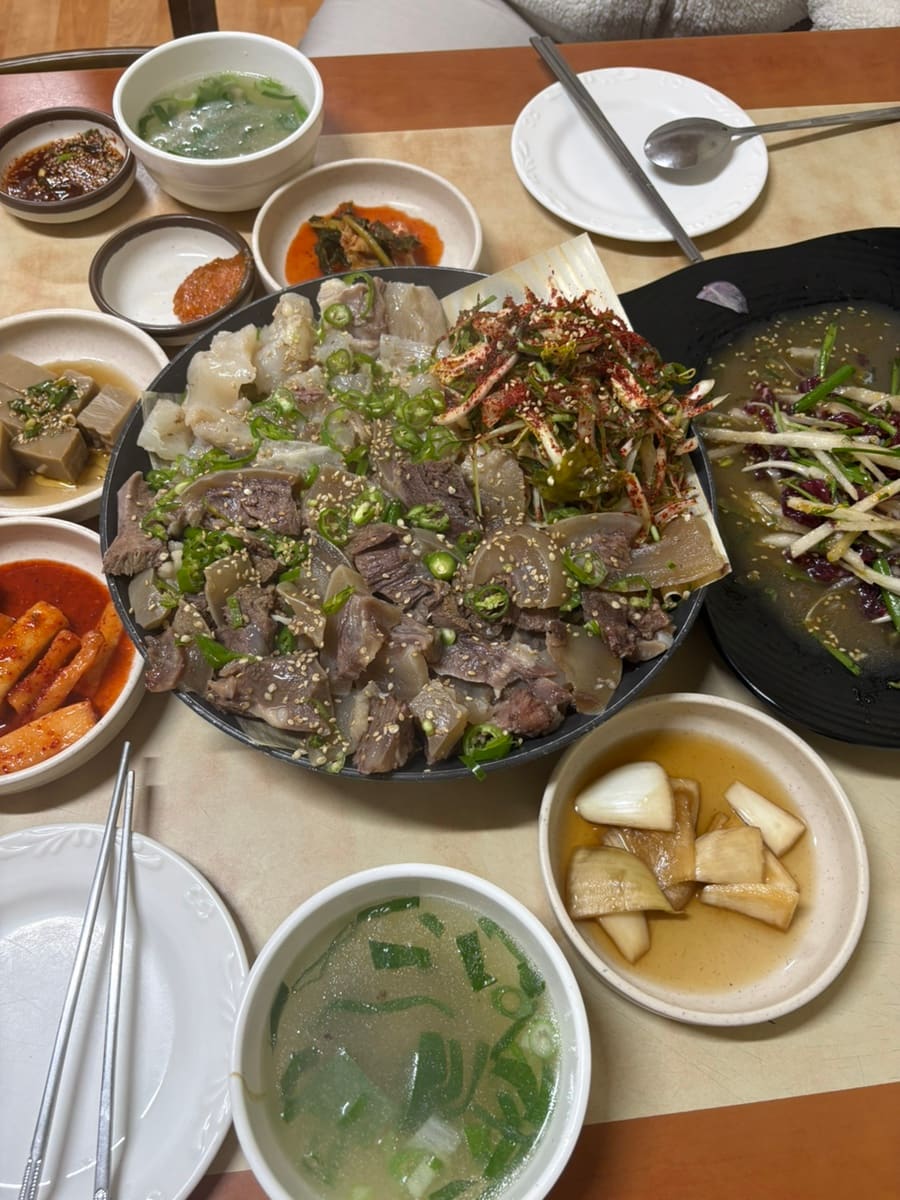 chxown이 담은 반반수육 접시와 한 상 전체입니다. 도가니와 소머리가 절반씩 나뉘어 쌓이고 그 위로 파무침과 깨가 넉넉히 얹혀 있으며, 곁으로 육회 무침과 맑은 탕 두 그릇,
