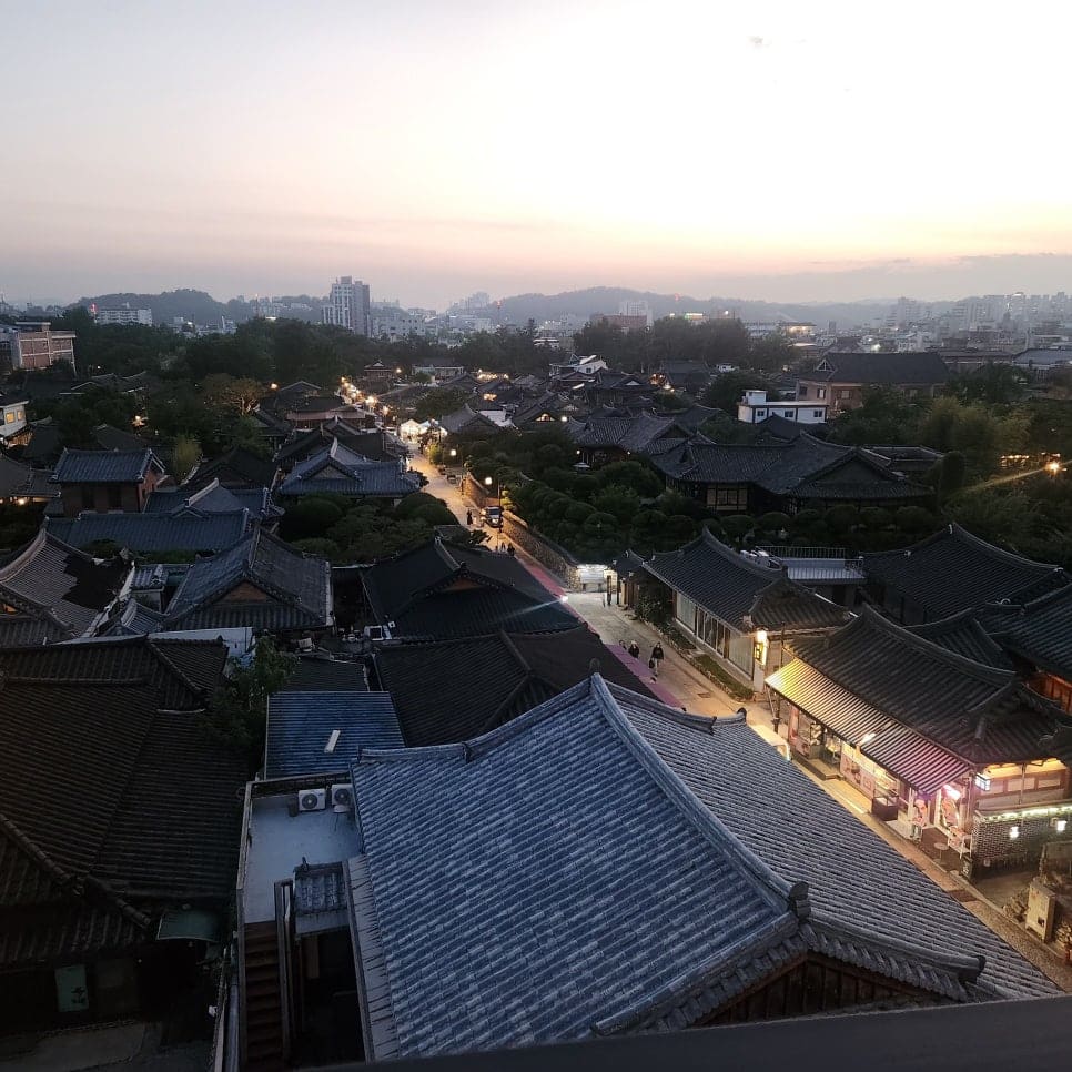 sma9995가 옥상 카페에서 찍은 한옥마을 지붕 전경입니다. 해질 무렵 검은 기와지붕이 파도처럼 이어지고, 그 사이로 조명이 켜진 골목길이 곧게 뻗어 있습니다.