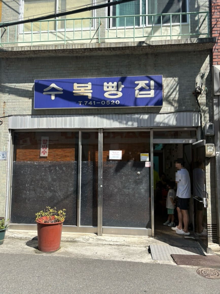 수복빵집 파란 간판과 붐비는 가게 안쪽 모습. 오래전부터 이 자리를 지켜온 빵집으로, 줄 선 손님들 사이에 아이를 데려온 가족도 보인다.