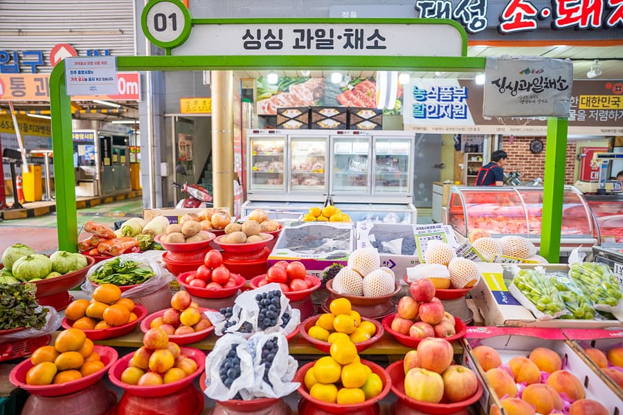 지붕 덮인 아케이드 통로 아래로 과일가게 좌판이 늘어서 있다. 매일 문을 여는 상설시장의 지금 모습을 보여준다.