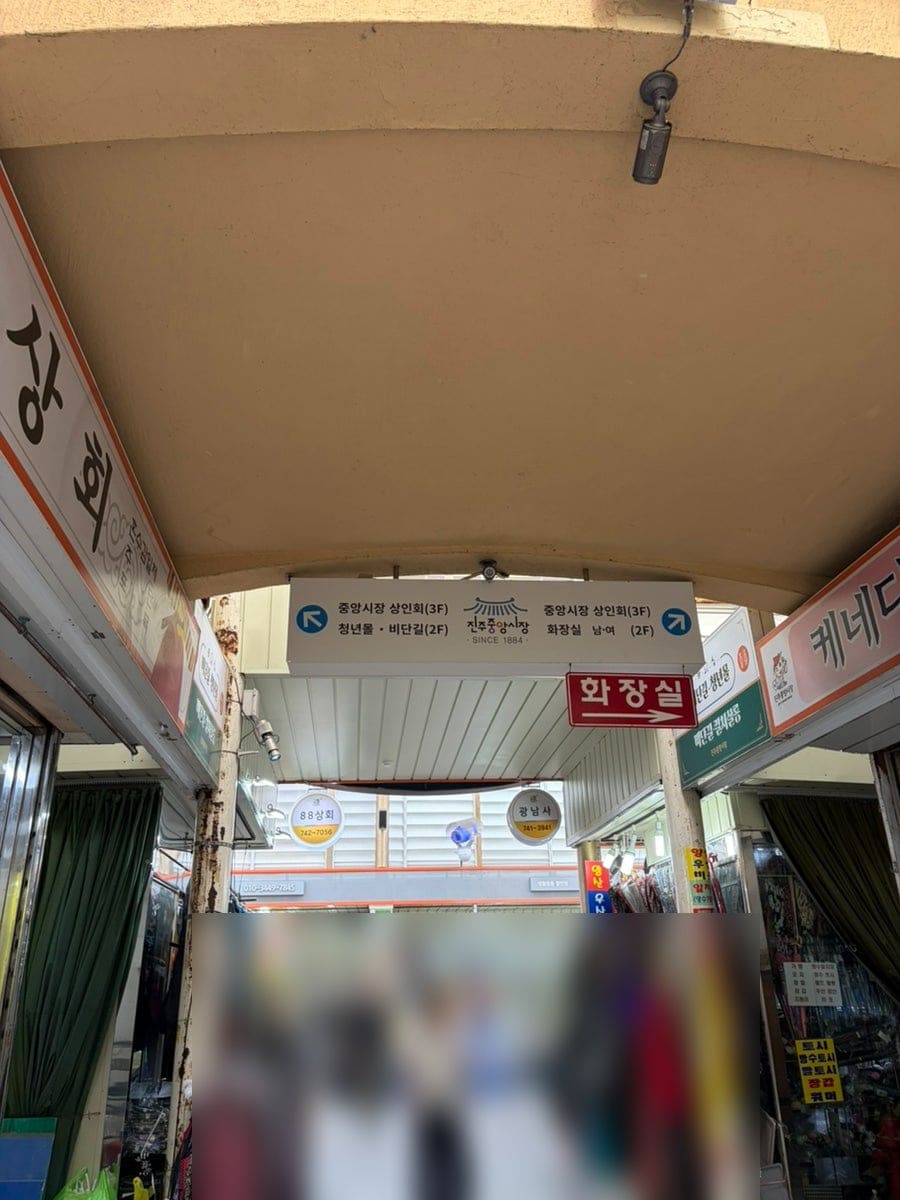 1884년을 새긴 진주중앙시장 표지판과, 상인회가 있는 3층과 청년몰 비단길이 있는 2층을 가리키는 안내판이다. 가격표시제를 알리는 현수막도 함께 걸려 있다.