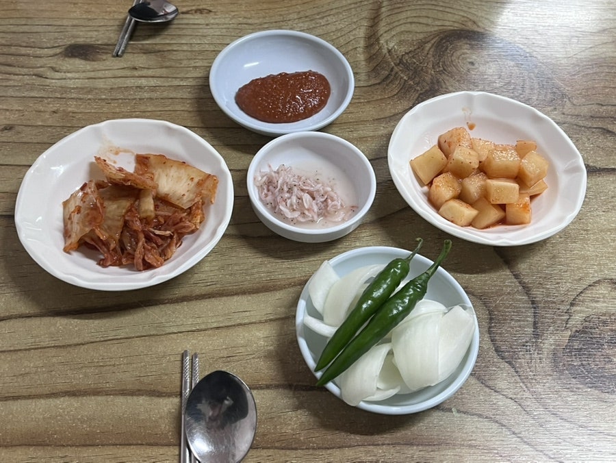 jjs1324는 저녁 무렵 불 켜진 간판과, 함께 나온 깍두기·양파 절임·매운 양념장 같은 밑반찬을 한 상에 담아 찍었습니다.