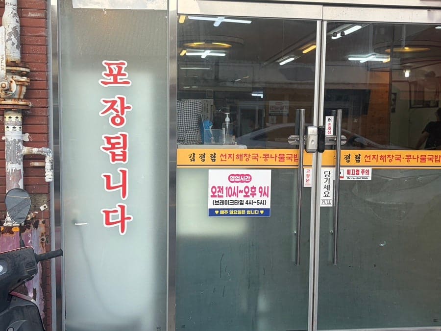 ka020486은 붉은 벽돌 건물에 걸린 노란 간판과 주황 어닝, 문 앞에 세워진 오토바이까지 정면에서 찍고, 유리문에 붙은 영업시간 안내문도 가까이서 찍었습니다.